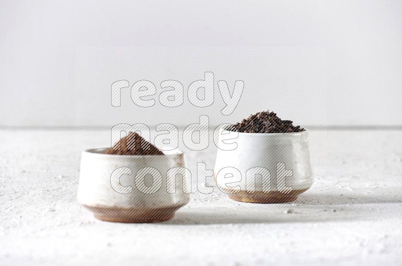 2 Beige ceramic bowls, one full of cloves and the other full of powder on textured white flooring