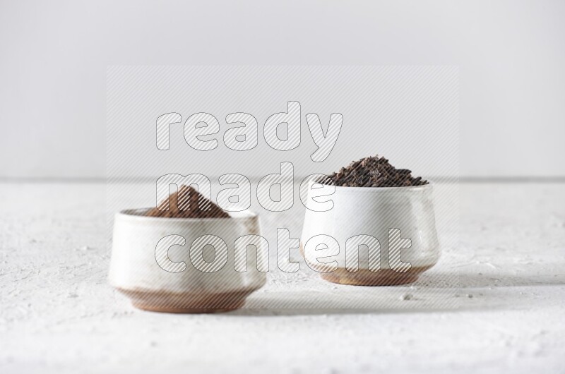 2 Beige ceramic bowls, one full of cloves and the other full of powder on textured white flooring