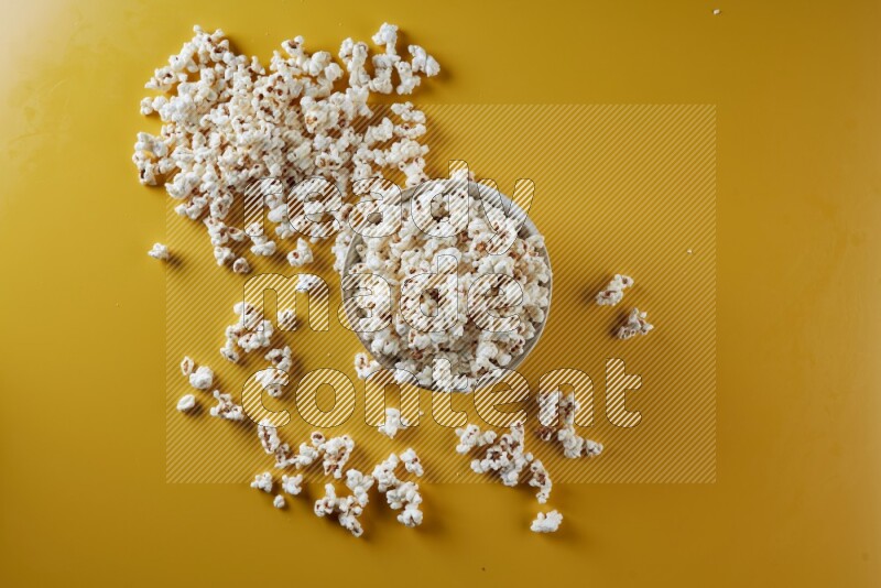 A white pottery bowl full of popcorn with popcorn beside it on a yellow background in different angles