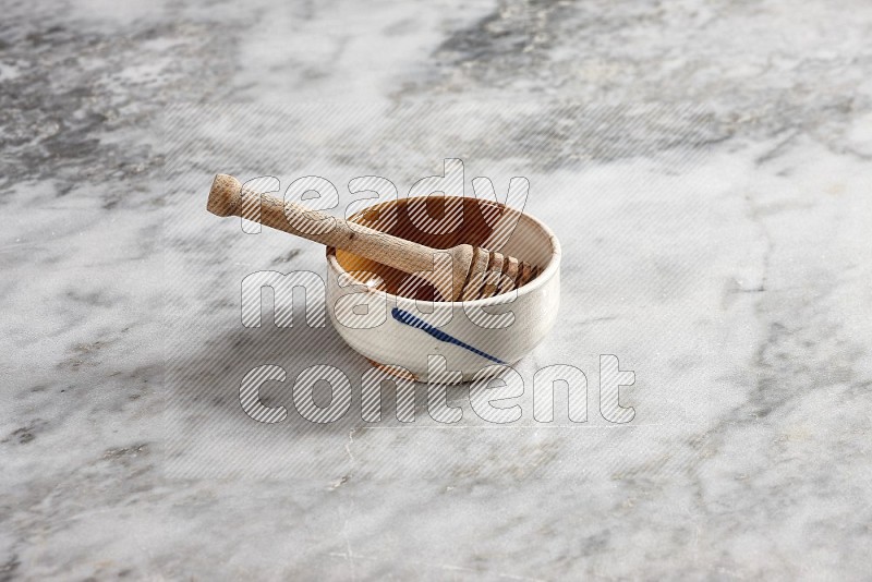 Multicolored Pottery bowl with wooden honey handle in it, on grey marble flooring, 45 degree angle