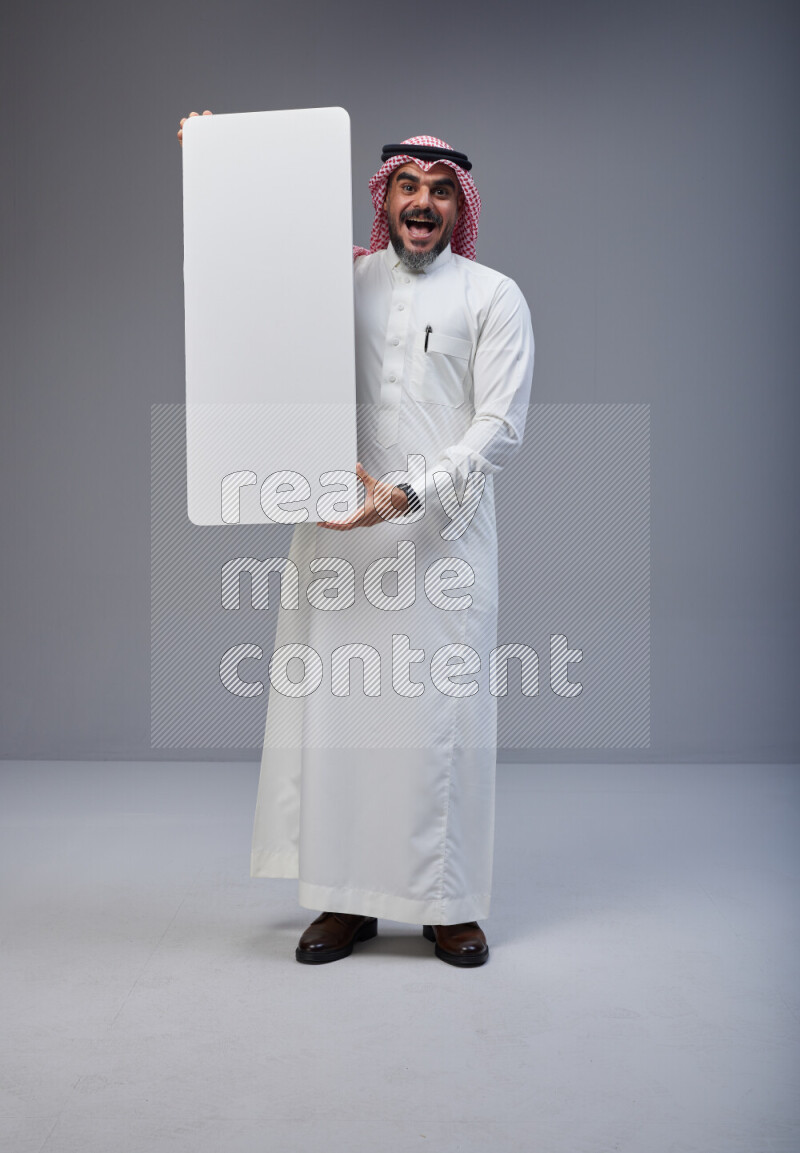 Saudi man Wearing Thob and red Shomag standing holding board on Gray background