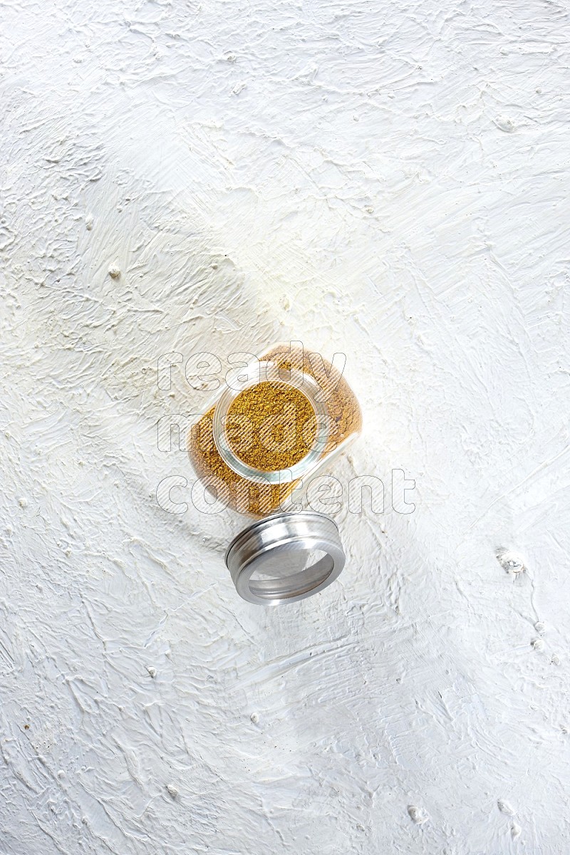 A glass spice jar full of turmeric powder on a textured white flooring