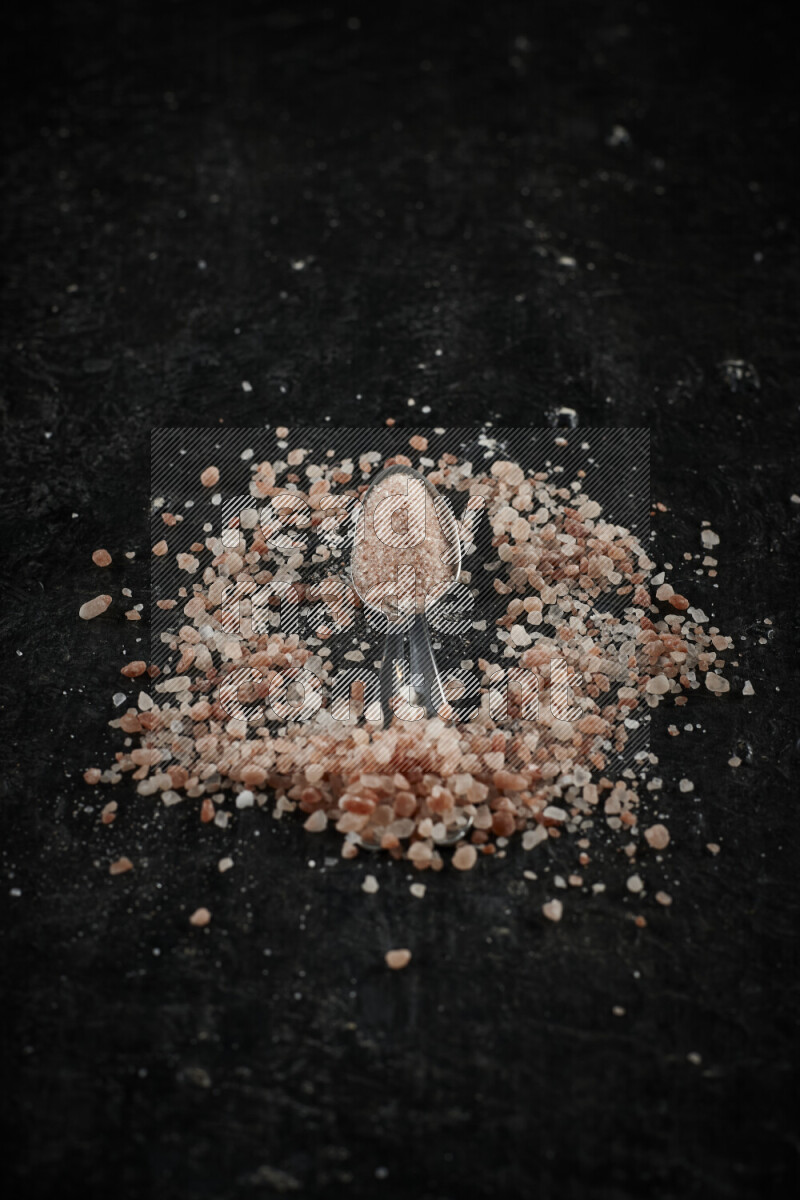 ملعقتان معدنيتان ممتلئتان بملح الهيمالايا الوردي على خلفية سوداء