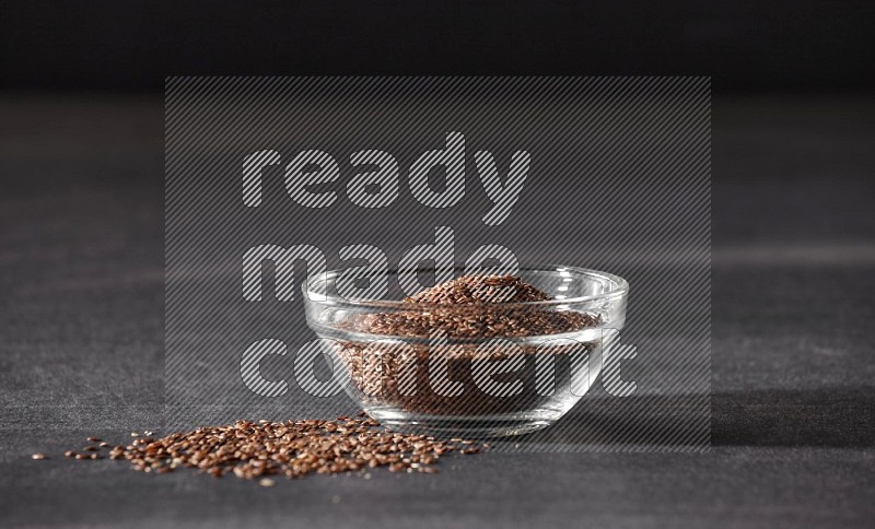 وعاء زجاجي ممتلئ بحبوب بذر الكتان محاط بالبذور على أرضية سوداء