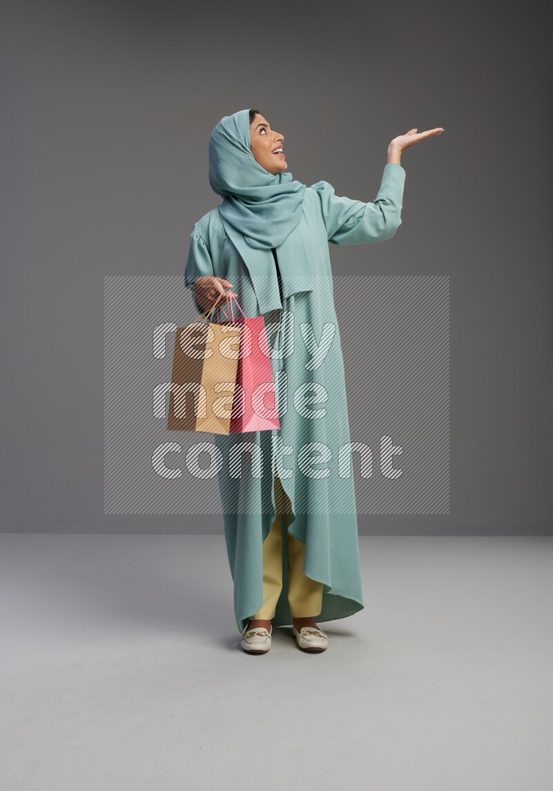 Saudi Woman wearing Abaya standing holding shopping bag on Gray background