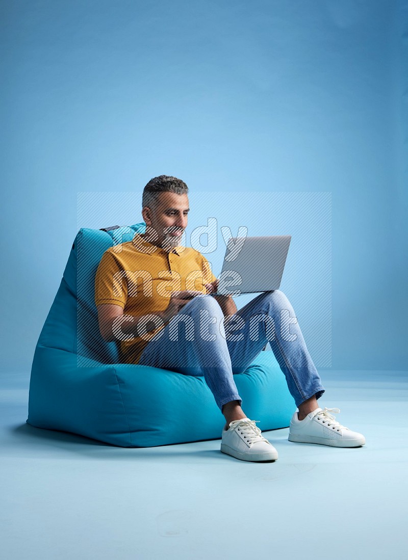 A man sitting on a blue beanbag and working on laptop