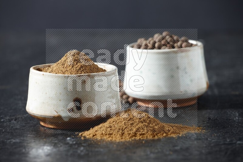 وعاءان بيج، أحدهما ممتلئ ببودرة بهار الفلفل الحلو والآخر بالحبوب وكلاهما متناثران على خلفية سوداء