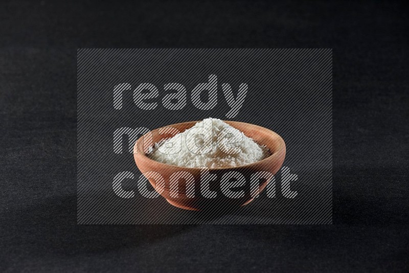 A wooden bowl full of desiccated coconut on a black background in different angles