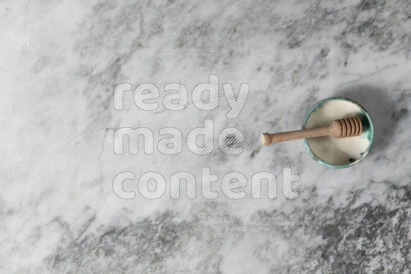 Multicolored pottery bowl with wooden honey dipper in it on grey marble background