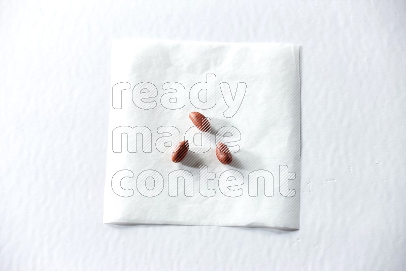 3 حبات من الفول السوداني على قطعة من الورق على خلفية بيضاء