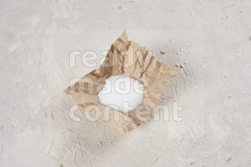 A crumpled piece of paper full of white salt on white background