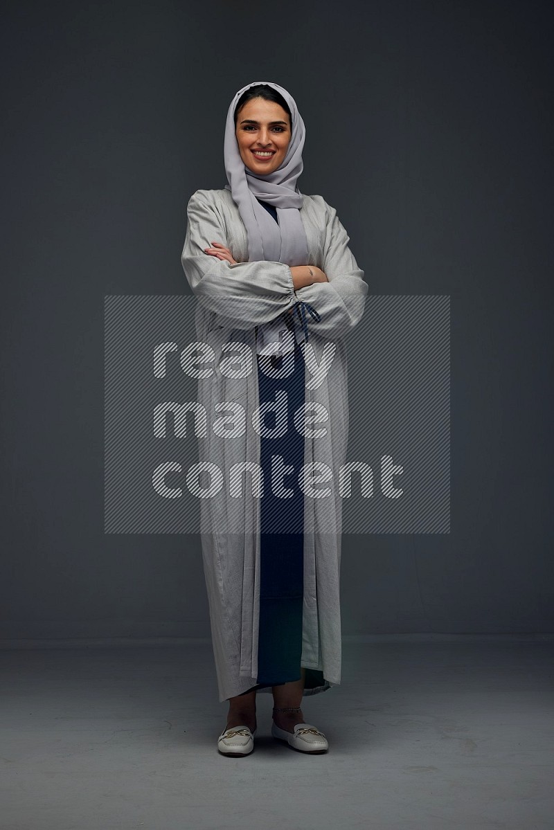 A Saudi woman wearing a light gray Abaya and head scarf standing and making multi poses eye level on a grey background