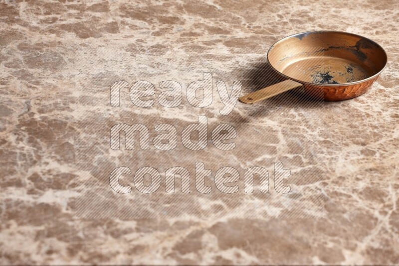 A small copper pan on beige marble background