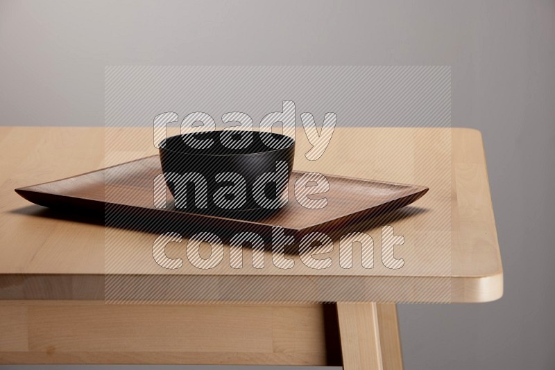 black bowl placed on a rectangular wooden tray on the edge of wooden table