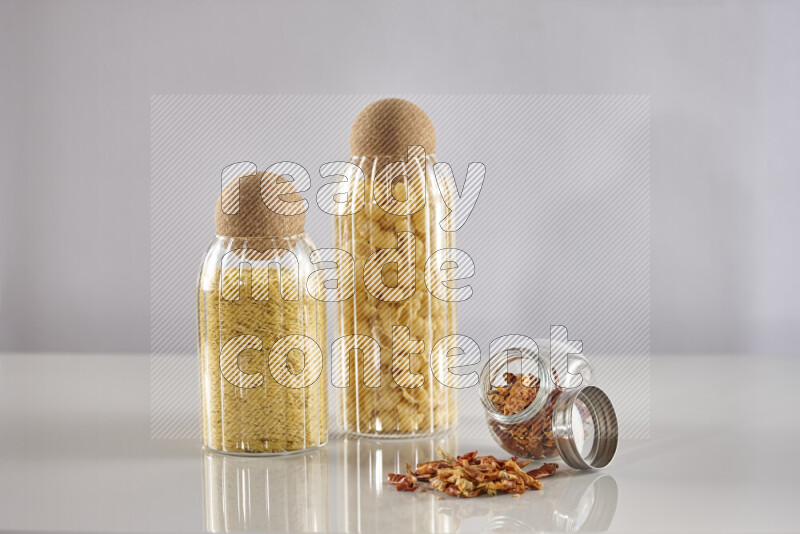 Raw pasta in glass jars with chilis on light grey background