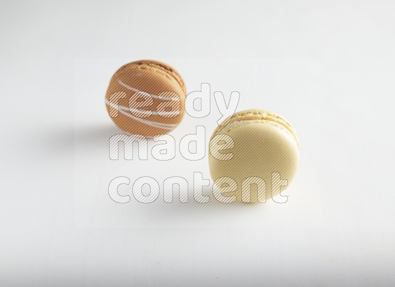 45º Shot of of two assorted Brown Irish Cream, and Yellow Vanilla macarons on white background