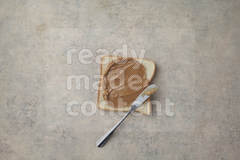 creamy peanut butter on a white toast with a spreading knife on a light blue textured background