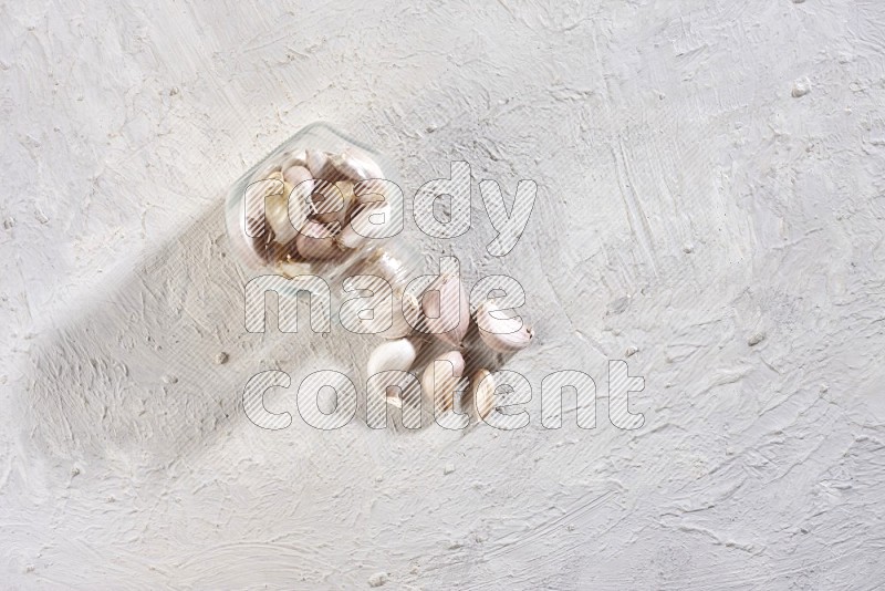 A glass spice jar full of garlic cloves flipped and the cloves came out on a textured white flooring in different angles