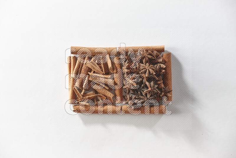 مربعان من أعواد القرفة ممتلئان باليانسون النجمي وقطع من القرفة علي خلفية بيضاء