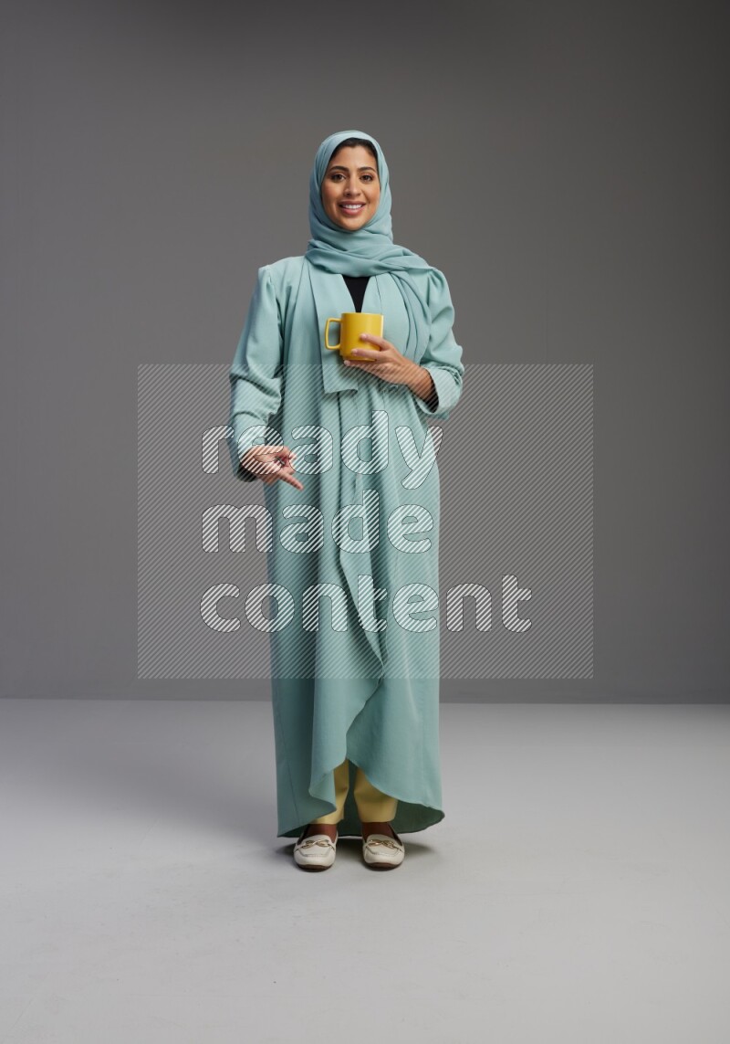 Saudi Woman wearing Abaya standing  holding a mug on Gray background