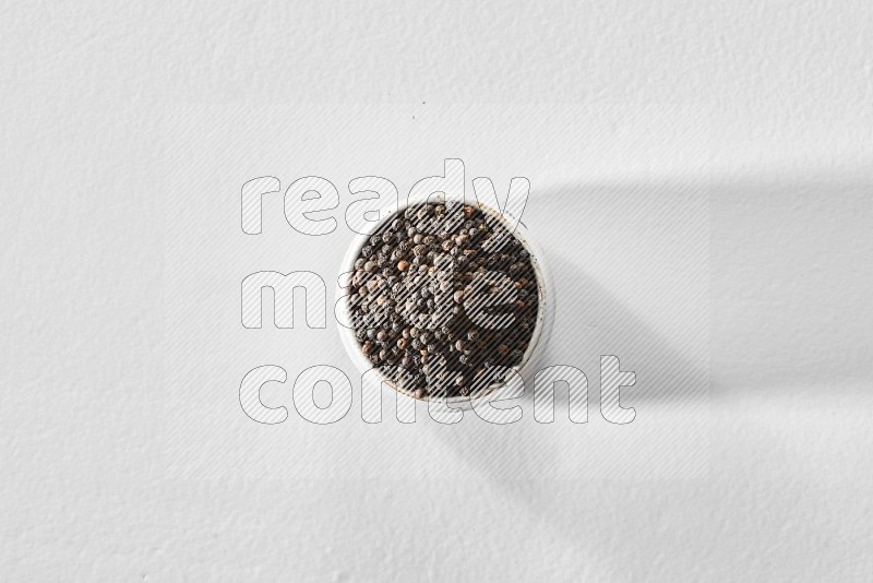 A white ceramic bowl full of black pepper on white flooring