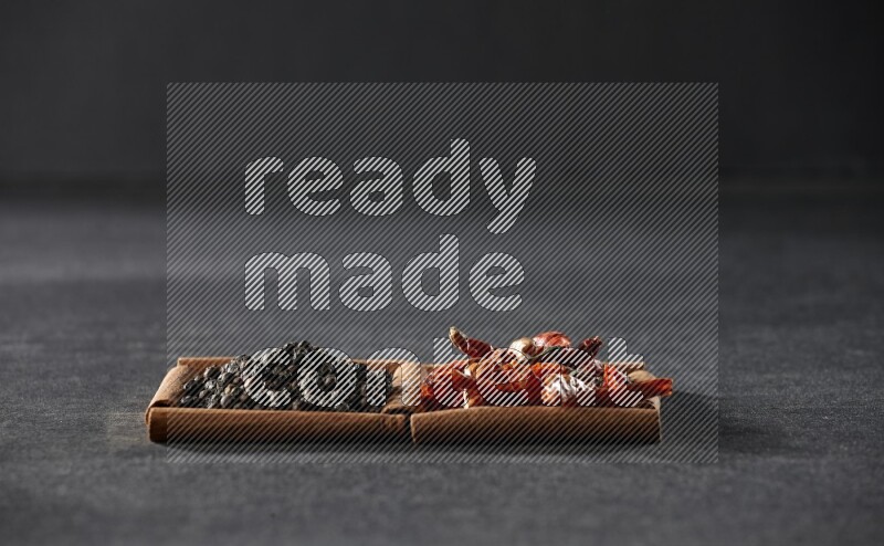 مربعان من أعواد القرفة ممتلئان بالفلفل الحار المجفف وحبوب الفلفل الأسود علي خلفية سوداء