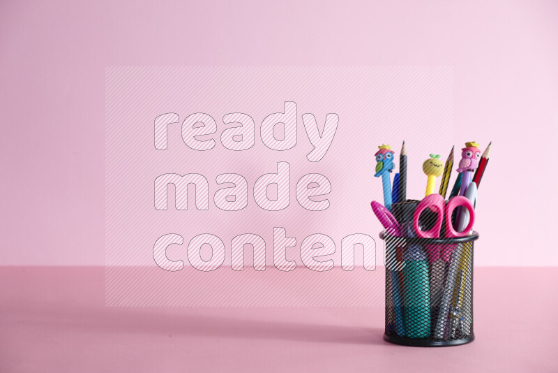 أقلام ومستلزمات مدرسية مختلفة أخري في حامل أقلام معدني على خلفية وردية