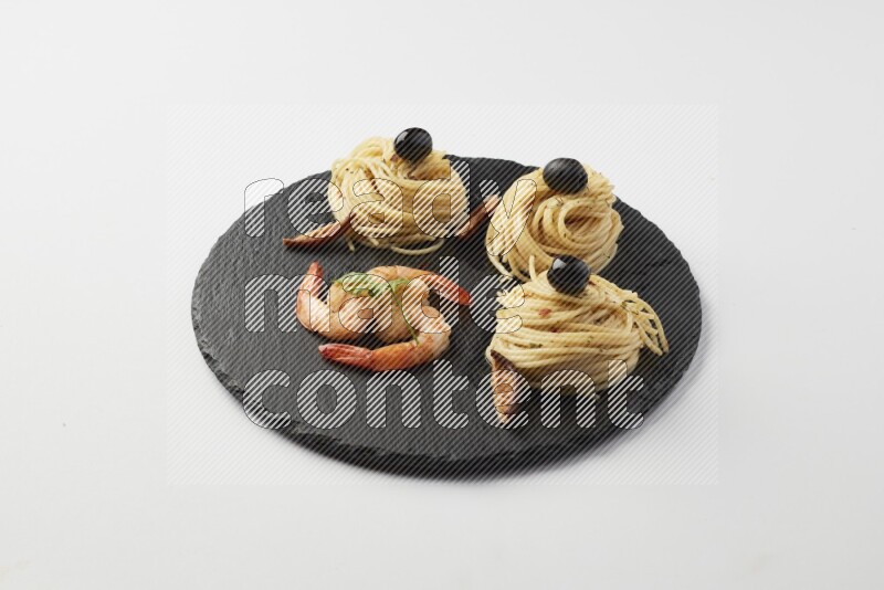 spaghetti nests with white sauce and shrimp on a black slate on a white background