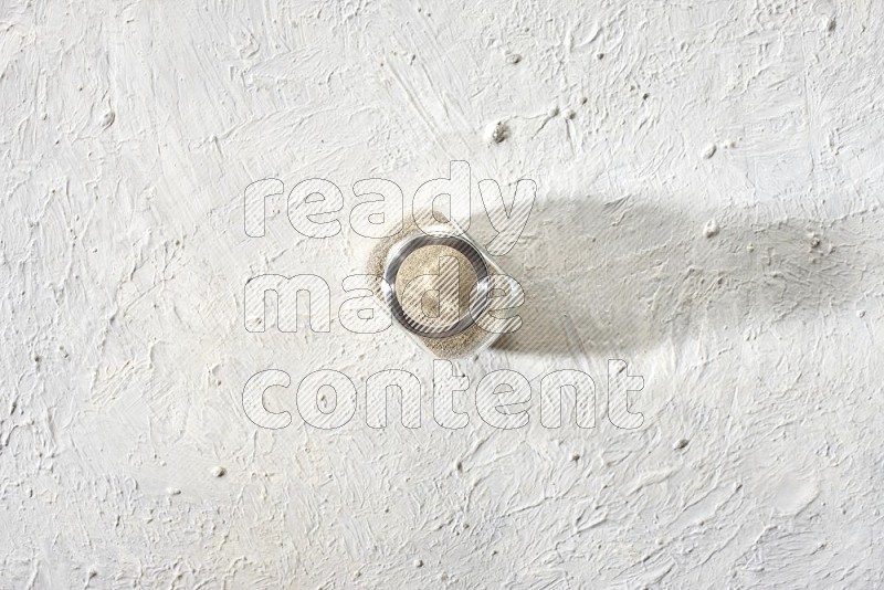 Herbal Glass jar full of white pepper powder on textured white flooring