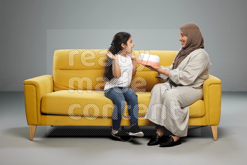 A girl sitting giving a cake to her mother on gray background