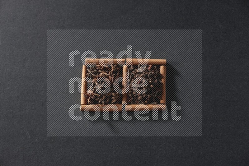 مربعان من أعواد القرفة ممتلئان باليانسون النجمي والقرنفل علي خلفية سوداء