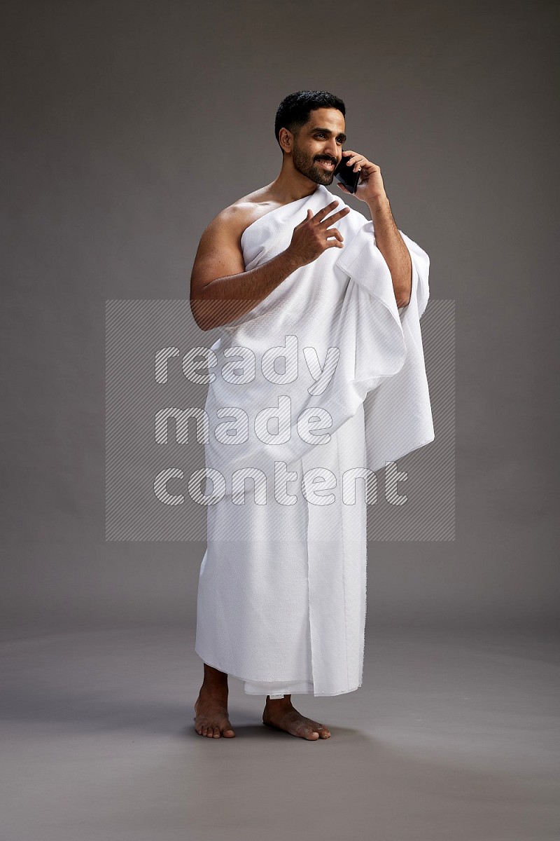 A man wearing Ehram Standing talking on phone on gray background