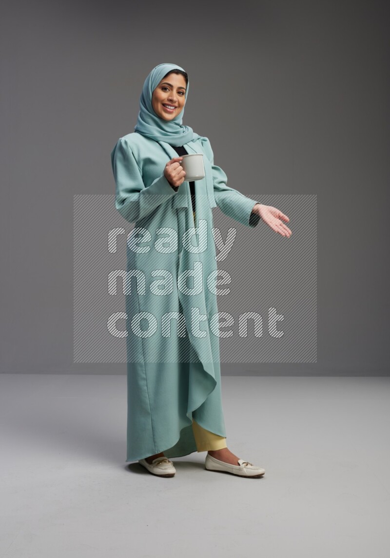 Saudi Woman wearing Abaya standing  holding a mug on Gray background