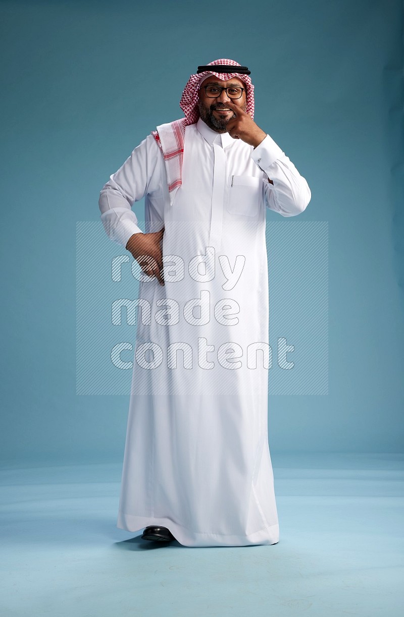 Saudi Man with shimag Standing Interacting with the camera on blue background