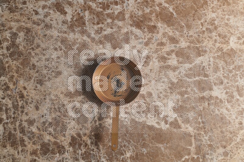 A small copper pan on beige marble background