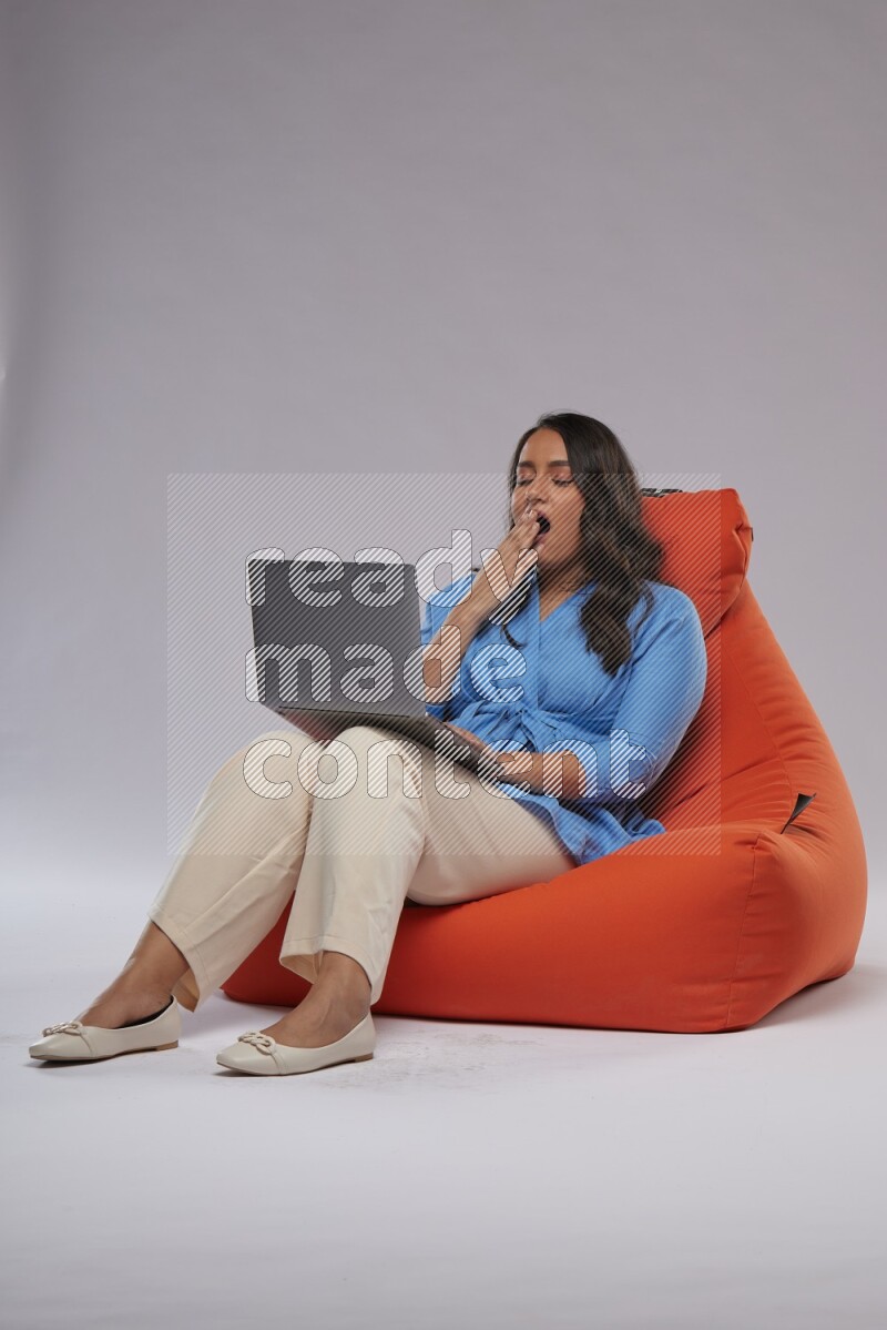 A woman sitting on an orange beanbag and working on laptop