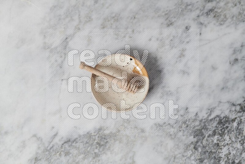 Multicolored pottery plate with wooden honey dipper in it on grey marble background
