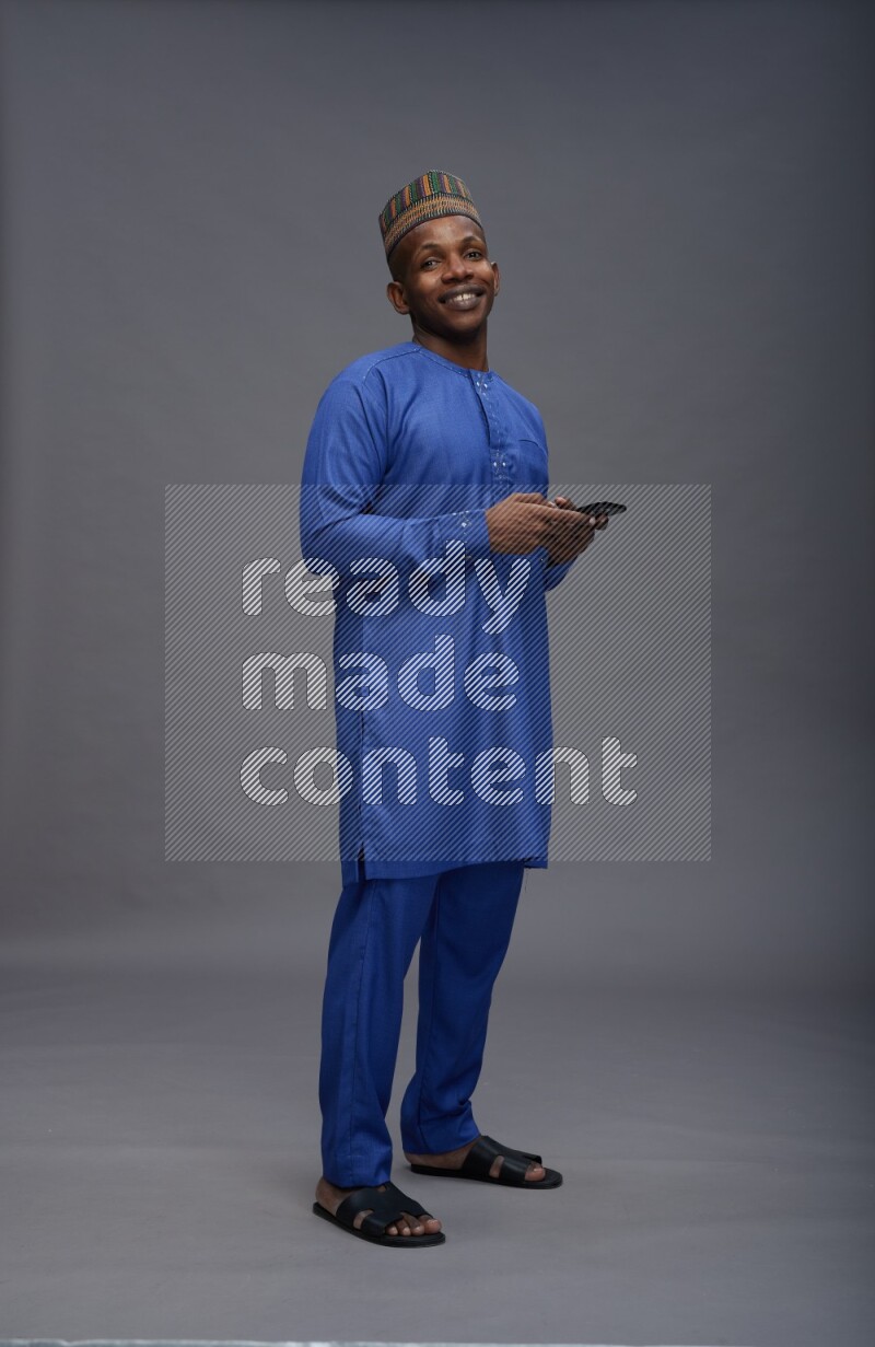 Man wearing Nigerian outfit standing texting on phone on gray background