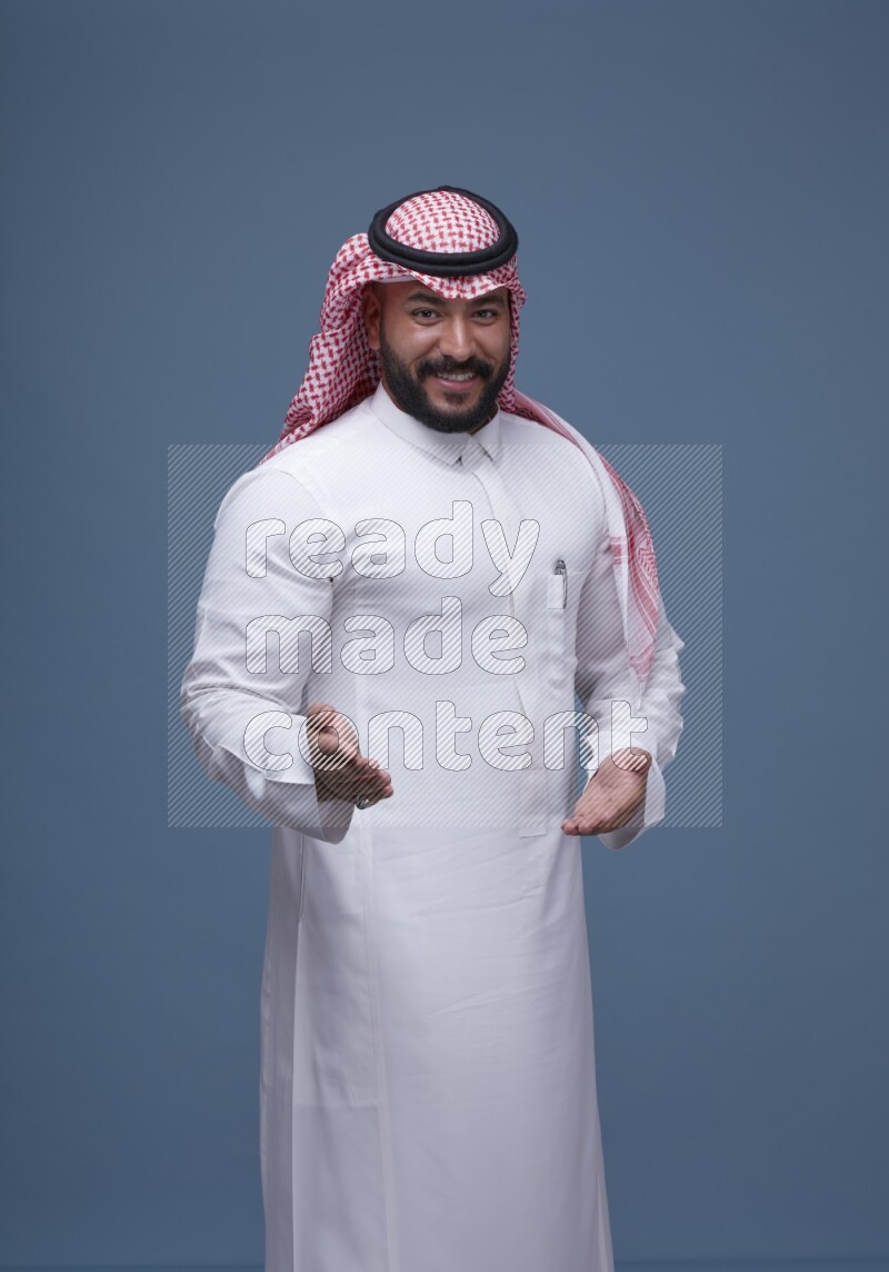 A man pointing on blue background wearing Saudi Thob with Shomag