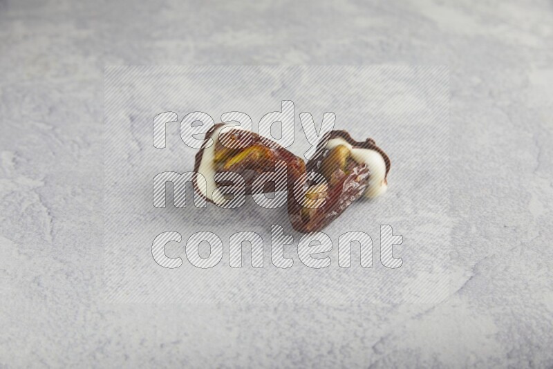 two pistachio stuffed dates covered with white chocolate with dark chocolate drizzle on a light grey background