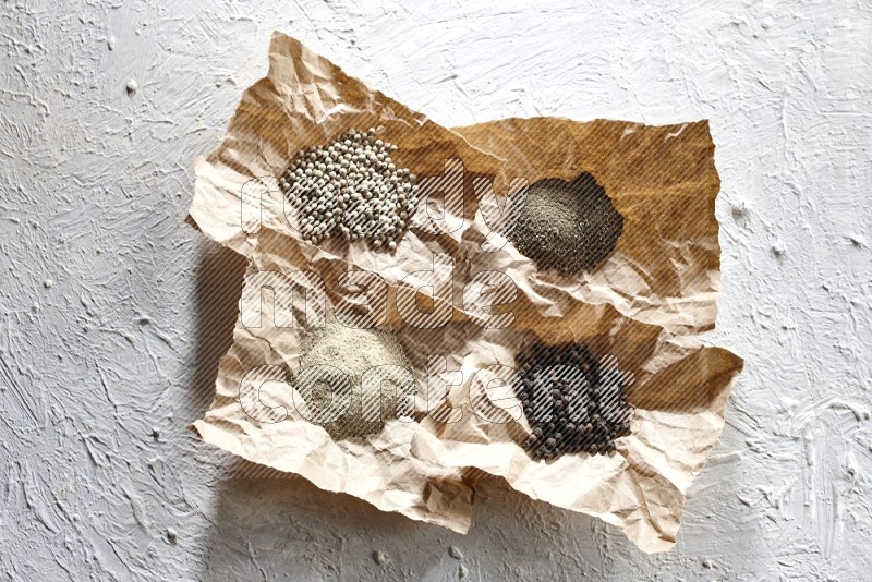 Crumpled pieces of paper full of black and white pepper beads and powder on a textured white flooring
