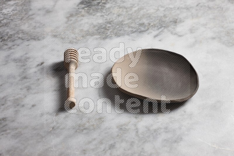 Multicolored pottery plate with wooden honey dipper on the side on grey marble background