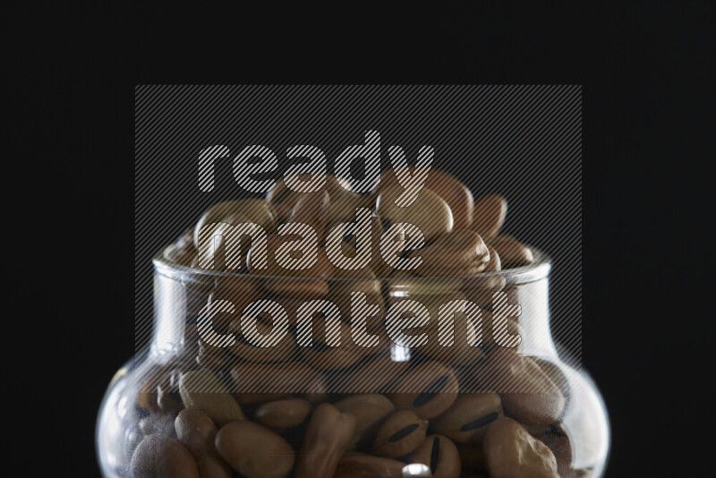 Fava beans in a glass jar on black background