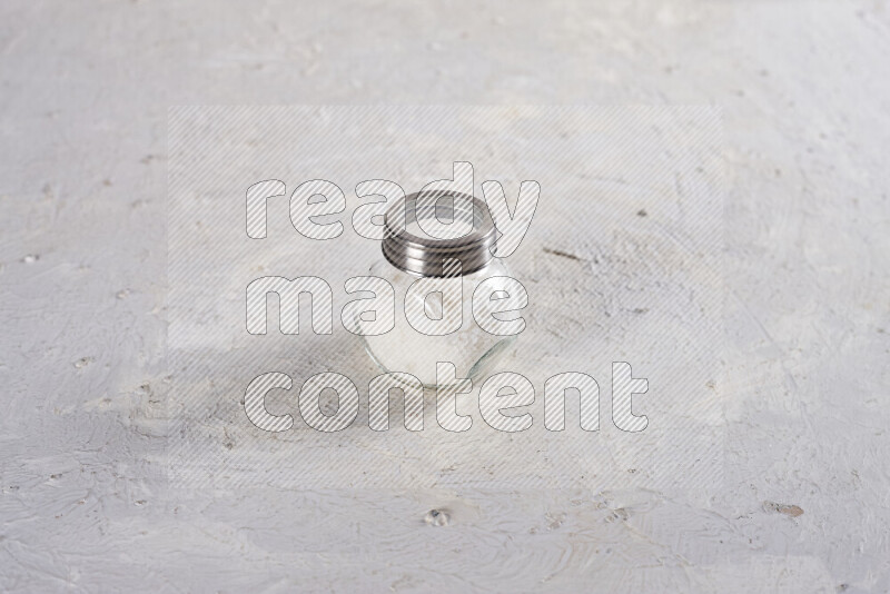 A glass jar full of coarse sea salt crystals on white background