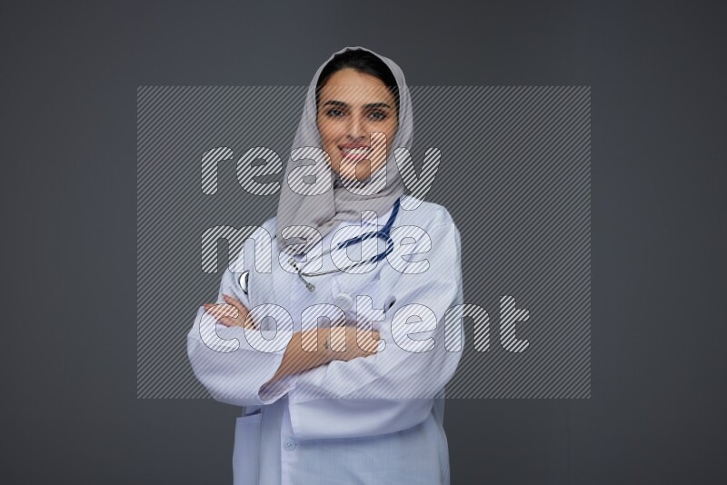 A female doctor wearing a light gray head scarf standing on grey background.