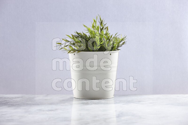 Green artificial plant in white pot on grey marble background