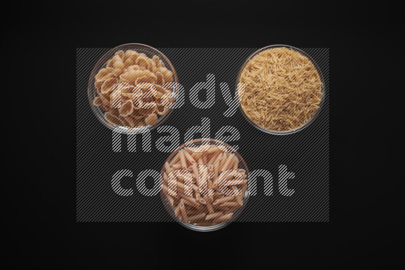 Different pasta types in glass bowls on black background