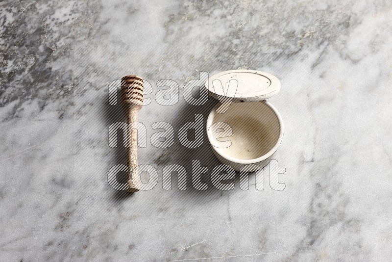 White Pottery bowl with wooden honey handle on the side with grey marble flooring, 65 degree angle