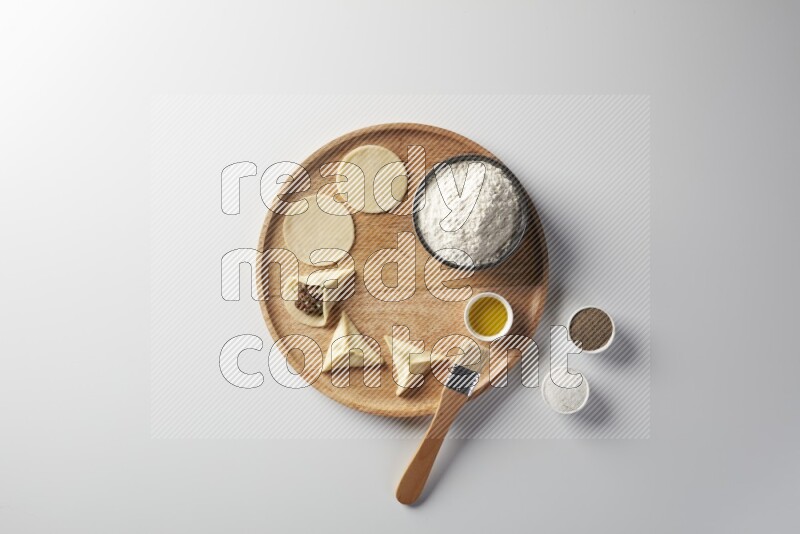 two closed sambosas and one open sambosa filled with meat while flour, salt, black pepper and oil with oil brush aside in a wooden dish on a white background