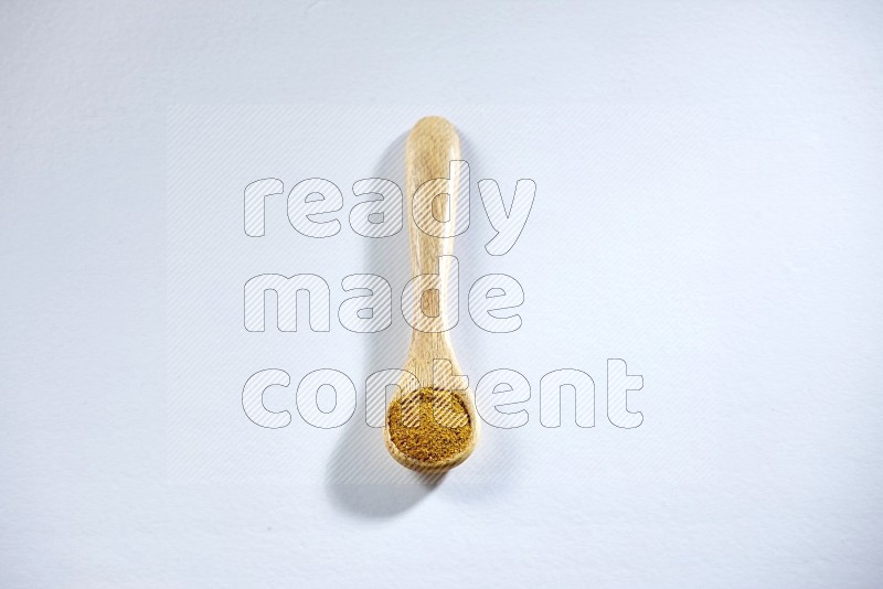 A wooden spoon full of turmeric powder on white flooring